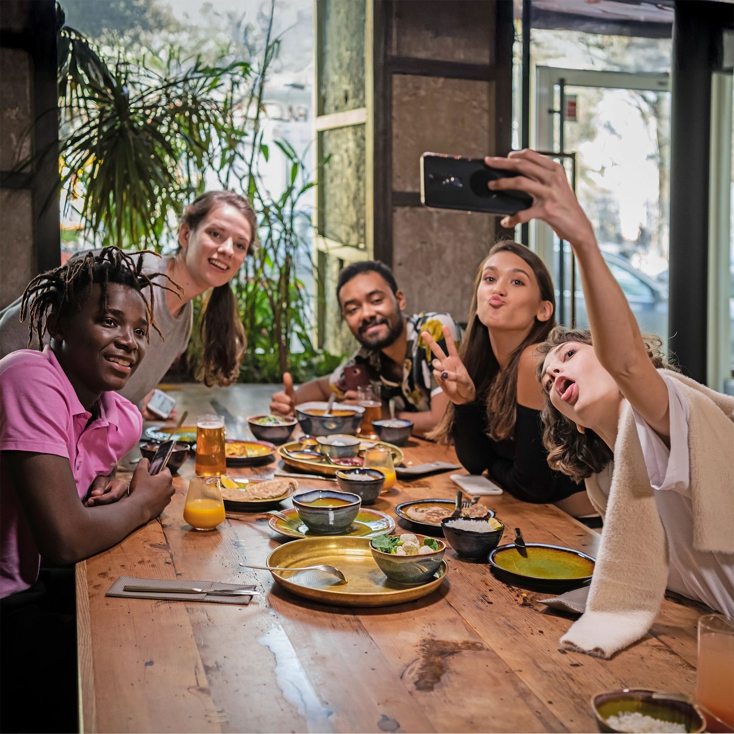 Eine Gruppe von Freunden sitze zusammen am gedeckten Tisch und macht ein Selfie