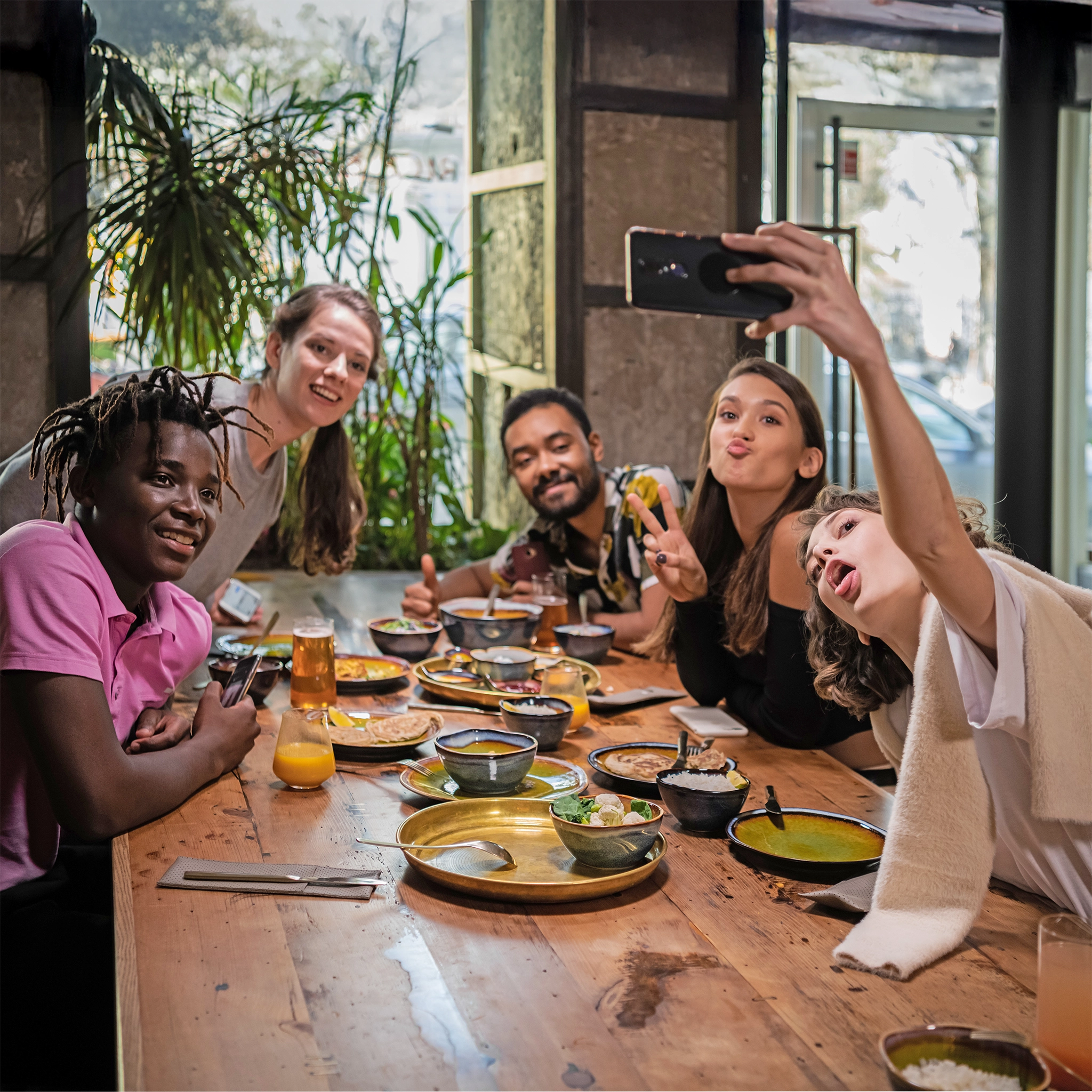 Eine Gruppe von Freunden sitze zusammen am gedeckten Tisch und macht ein Selfie