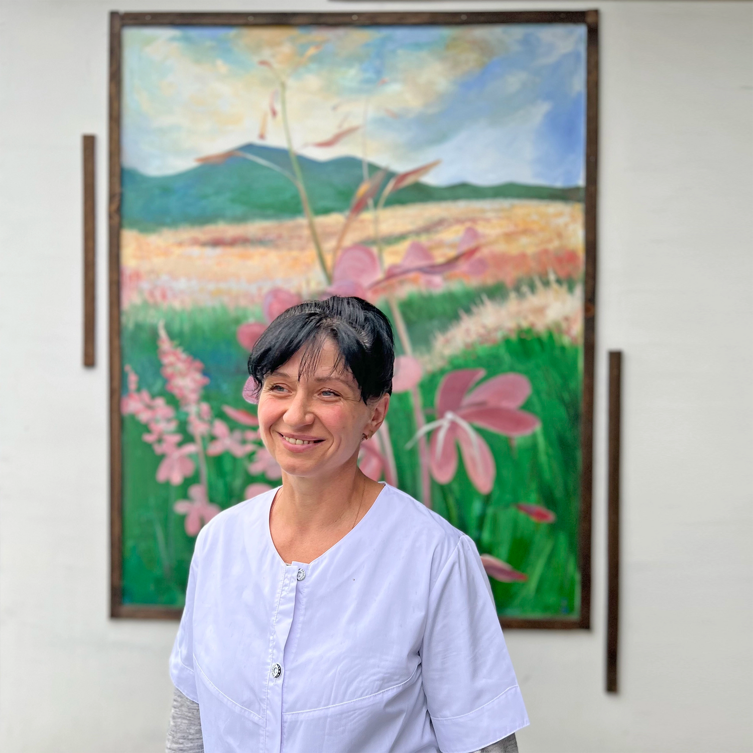 Eine Frau mit weißem Arbeitskittel steht vor dem Bild eines Weidenröschens