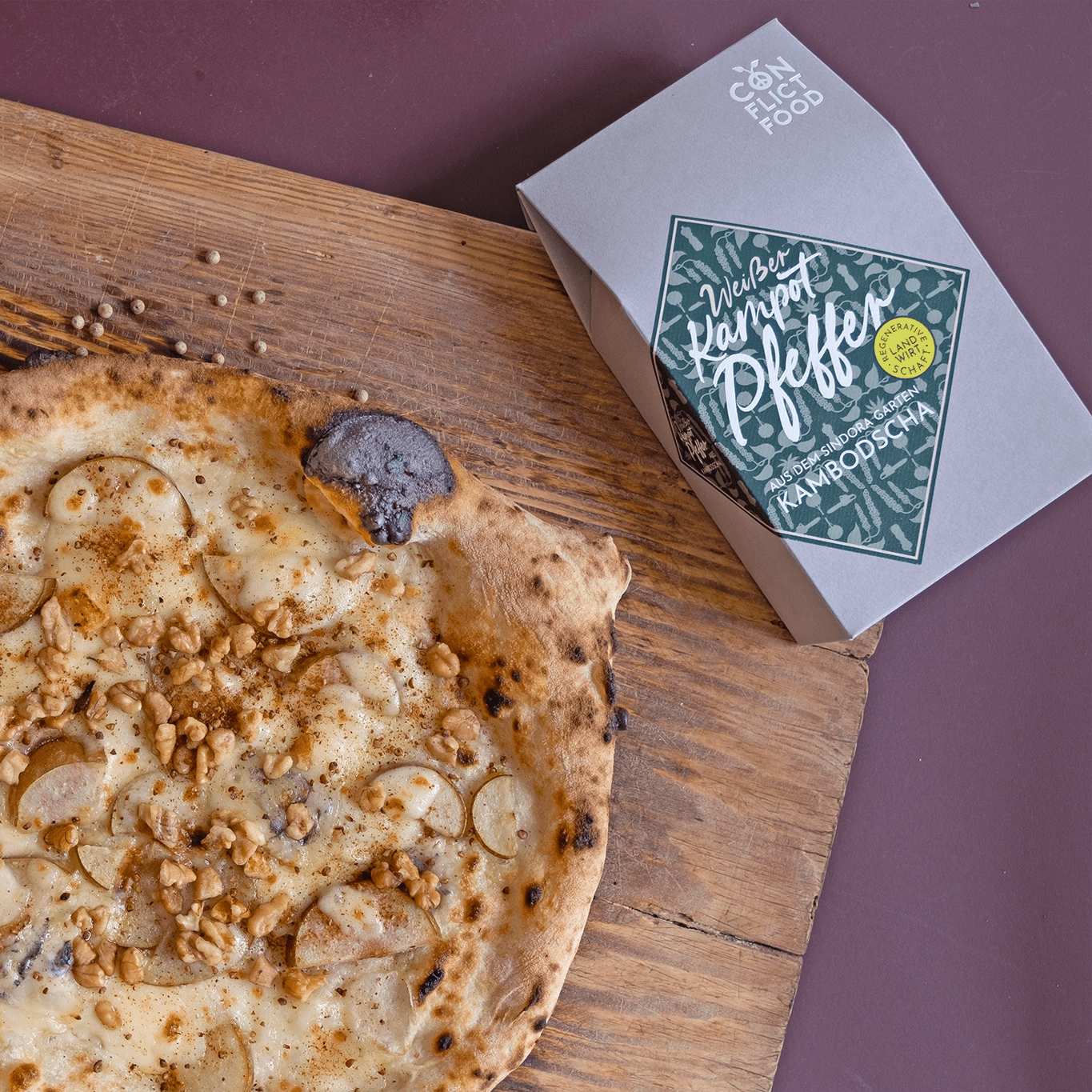 Eine Pizza mit Birne und Gorgonzola, daneben eine Packung Kampot Pfeffer von Conflictfood