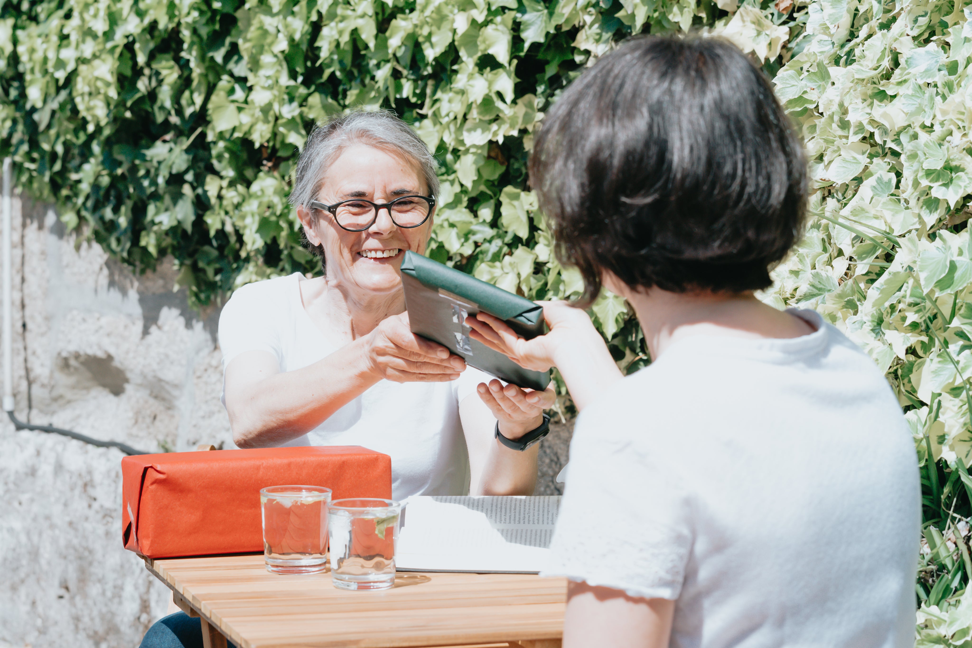Eine Dame überreicht einer anderen Dame ein verpacktes Geschenk