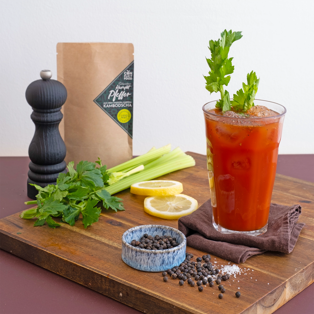 Ein Glas mit roter Bloody Marry und Eiswürfel sowie Kampot Pfeffer und Stangensellerie