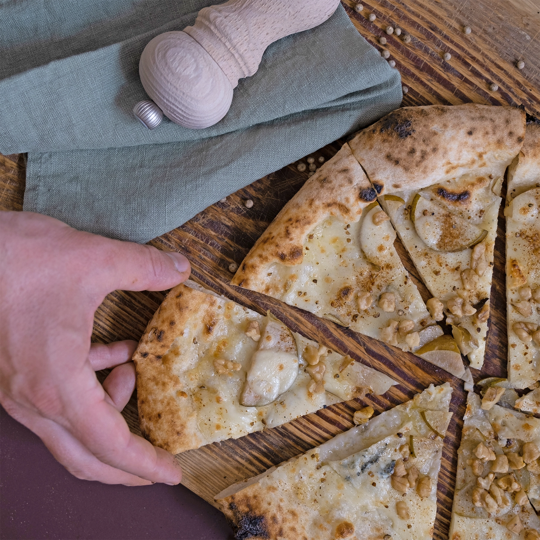 Eine Hand greift nach einem Stück Pizza mit Birne und Gorgonzola
