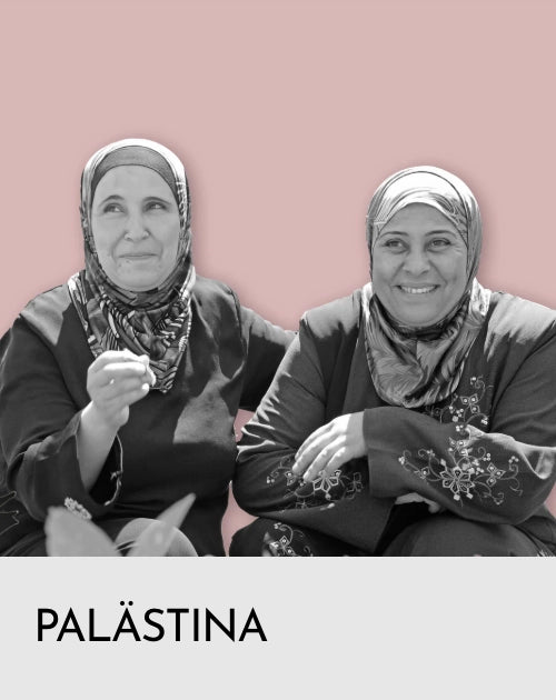 Zwei lächelnde Frauen mit bestickten Kleidern und Hidjab / Kopftuch .
Darunter weißer Balken mit Schrift Palästina