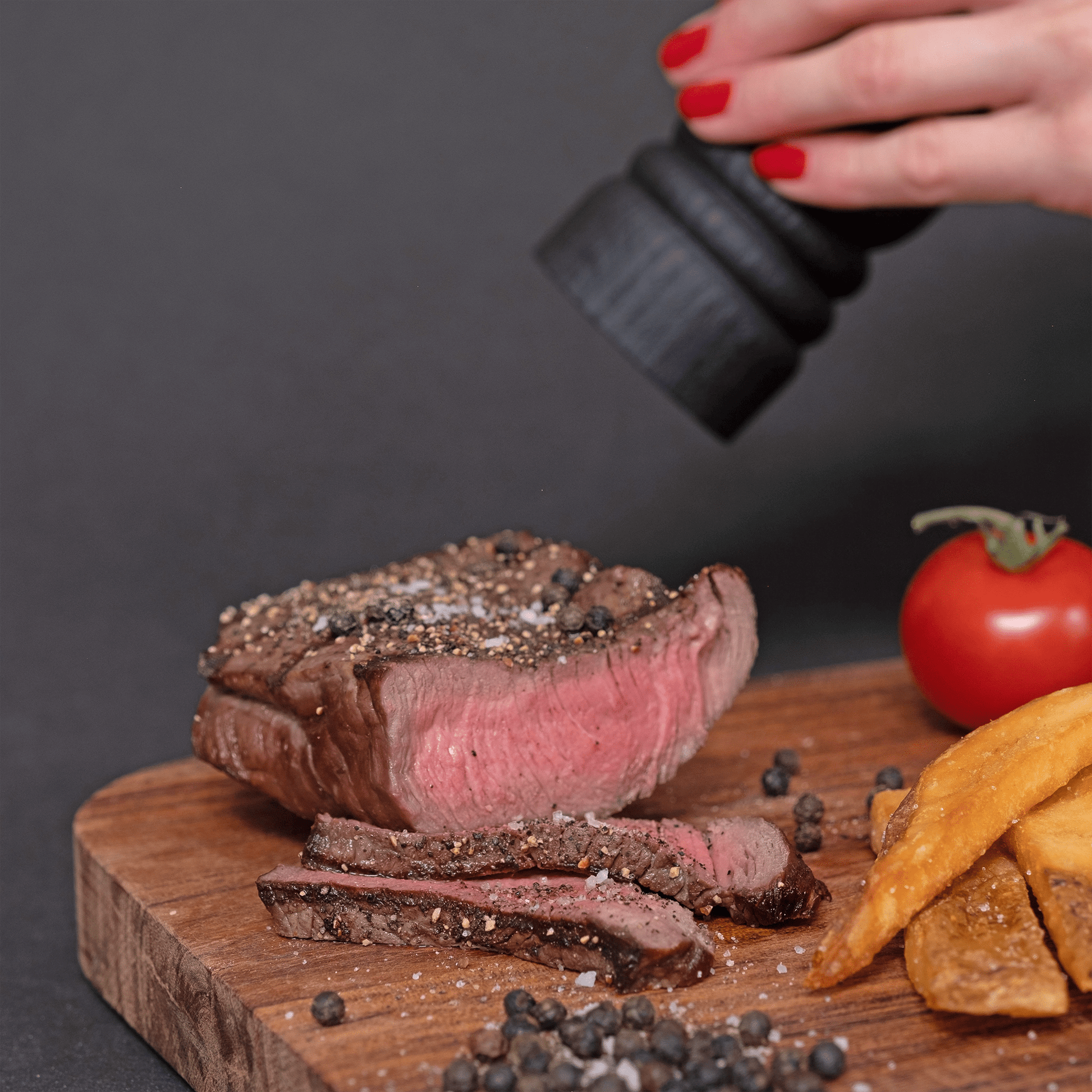 Ein saftiges Steak wird mit einer Pfeffermühle gewürzt und schwarzer Kampot Pfeffer liegt daneben