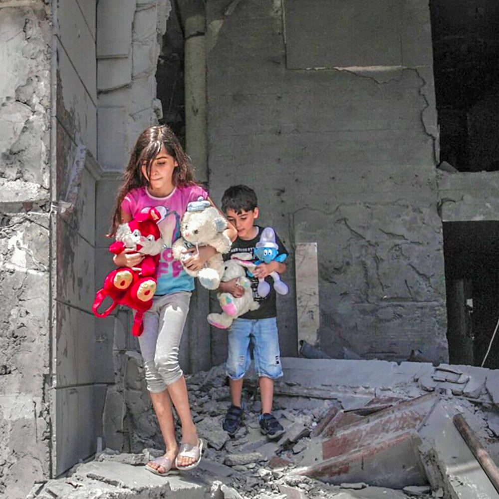 Eine Gruppe von Kindern mit Teddybären in der Hand flieht durch zerbombte Häuser